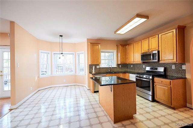 kitchen featuring tasteful backsplash, stainless steel appliances, sink, decorative light fixtures, and a center island