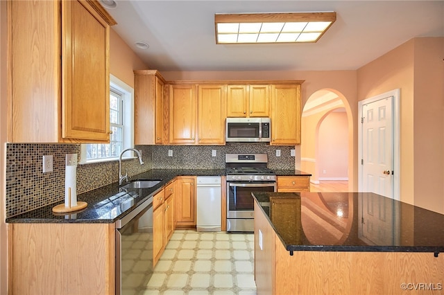 kitchen featuring decorative backsplash, appliances with stainless steel finishes, dark stone counters, sink, and a center island