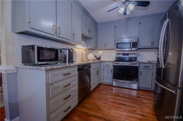 kitchen with decorative backsplash, dark hardwood / wood-style flooring, light stone counters, stainless steel appliances, and ceiling fan