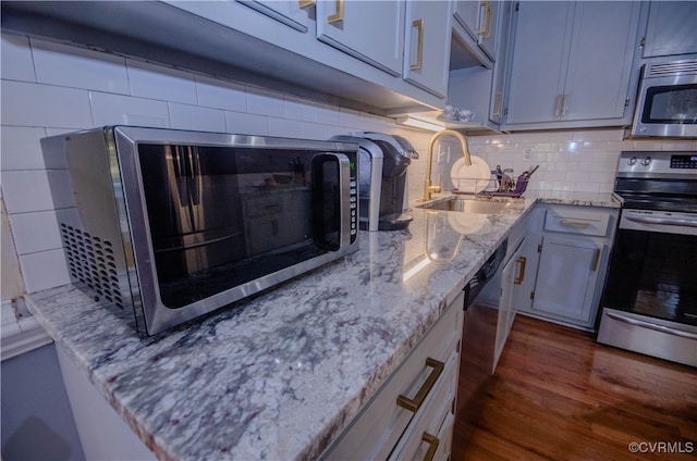 kitchen featuring decorative backsplash, appliances with stainless steel finishes, dark hardwood / wood-style flooring, light stone countertops, and sink