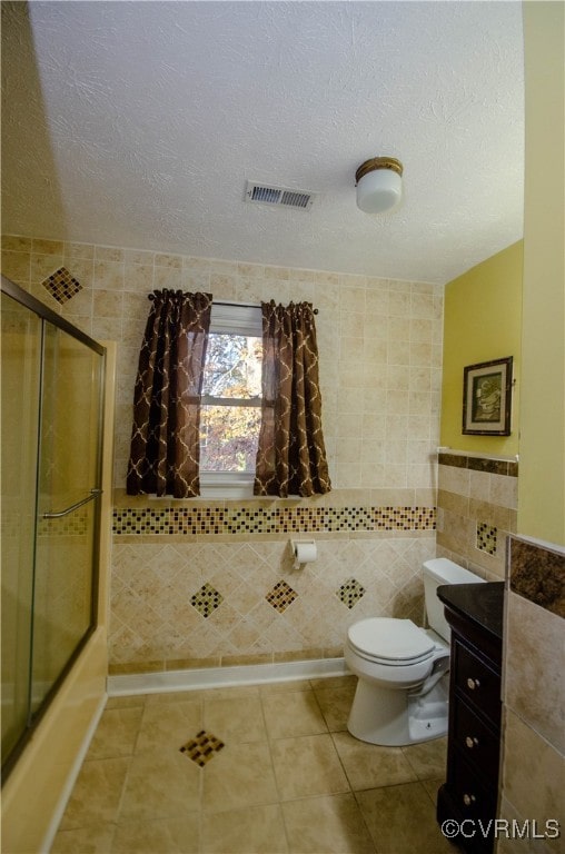 full bathroom with a textured ceiling, tile patterned flooring, bath / shower combo with glass door, and tile walls