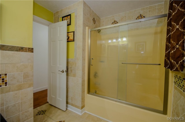 bathroom featuring a textured ceiling, tile patterned floors, tile walls, and bath / shower combo with glass door