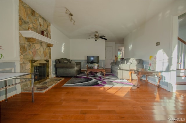 living room featuring rail lighting, vaulted ceiling, ceiling fan, hardwood / wood-style floors, and a stone fireplace