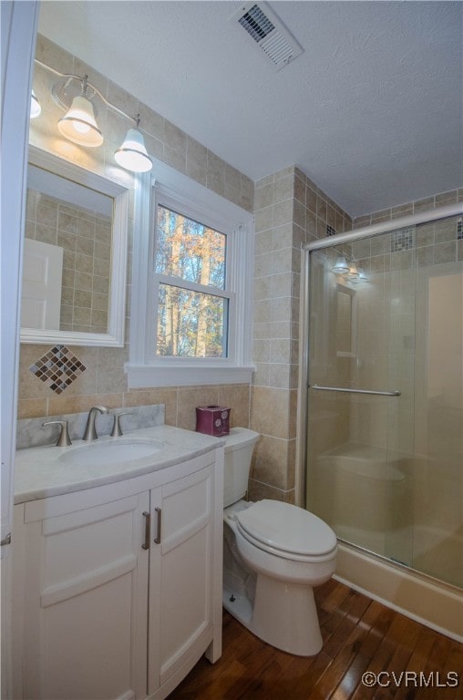 bathroom with toilet, an enclosed shower, tile walls, and hardwood / wood-style flooring