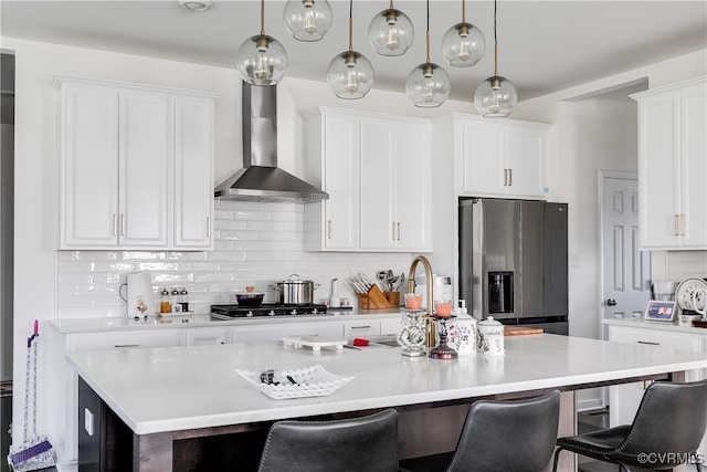 kitchen with wall chimney exhaust hood, stainless steel appliances, a center island with sink, white cabinets, and a breakfast bar area