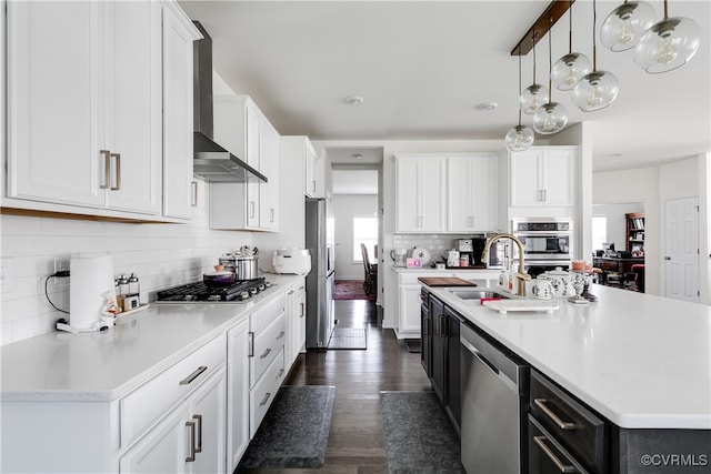 kitchen featuring appliances with stainless steel finishes, wall chimney exhaust hood, dark wood-type flooring, decorative light fixtures, and white cabinetry