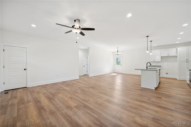 unfurnished living room with light hardwood / wood-style flooring, ceiling fan with notable chandelier, and sink