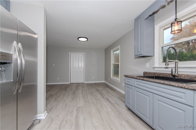 kitchen with sink, stainless steel refrigerator with ice dispenser, gray cabinets, light wood-type flooring, and decorative light fixtures