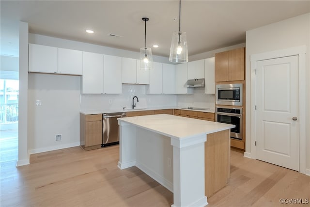 kitchen featuring white cabinets, stainless steel appliances, a kitchen island, and light hardwood / wood-style floors