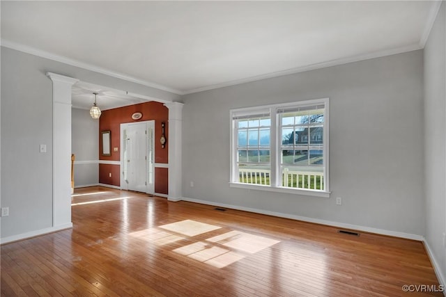 spare room with a chandelier, ornate columns, crown molding, and light hardwood / wood-style flooring