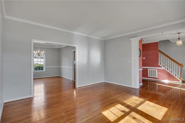 spare room with a chandelier, hardwood / wood-style floors, decorative columns, and crown molding