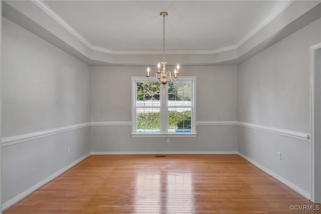 unfurnished room with a raised ceiling, crown molding, wood-type flooring, and an inviting chandelier