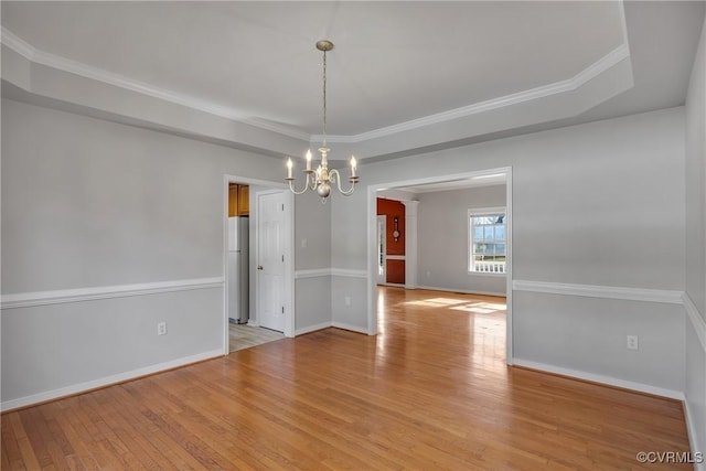 unfurnished dining area featuring an inviting chandelier, crown molding, a tray ceiling, and light hardwood / wood-style flooring