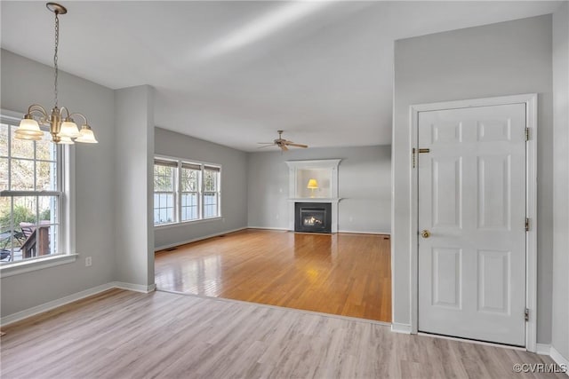 unfurnished living room with ceiling fan with notable chandelier and light hardwood / wood-style flooring