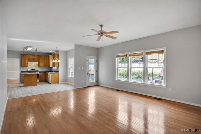 unfurnished living room with ceiling fan with notable chandelier and light hardwood / wood-style floors