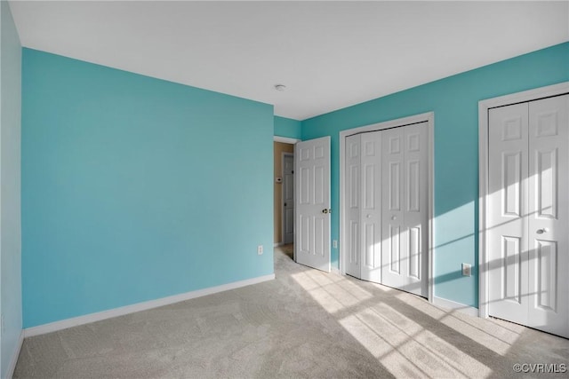 unfurnished bedroom with two closets and light colored carpet