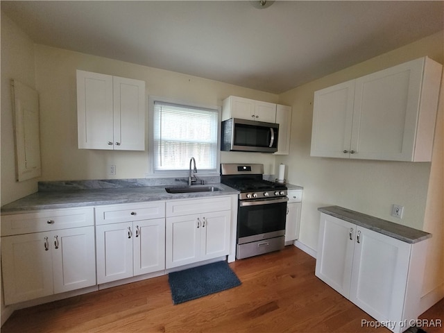 kitchen featuring wood-type flooring, stainless steel appliances, white cabinetry, and sink