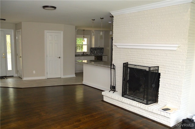 unfurnished living room featuring dark hardwood / wood-style floors, ornamental molding, sink, and a brick fireplace