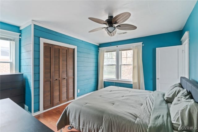 bedroom with hardwood / wood-style floors, a closet, wood walls, and ceiling fan