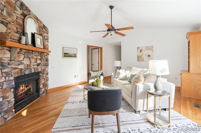 living room with a stone fireplace, ceiling fan, light hardwood / wood-style floors, and vaulted ceiling