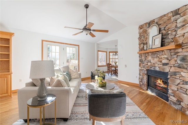 living room featuring a stone fireplace, ceiling fan, light hardwood / wood-style floors, and vaulted ceiling