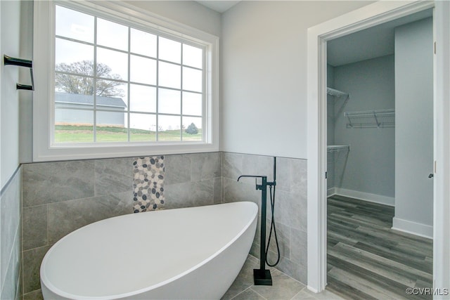 bathroom with a bath, hardwood / wood-style flooring, a wealth of natural light, and tile walls