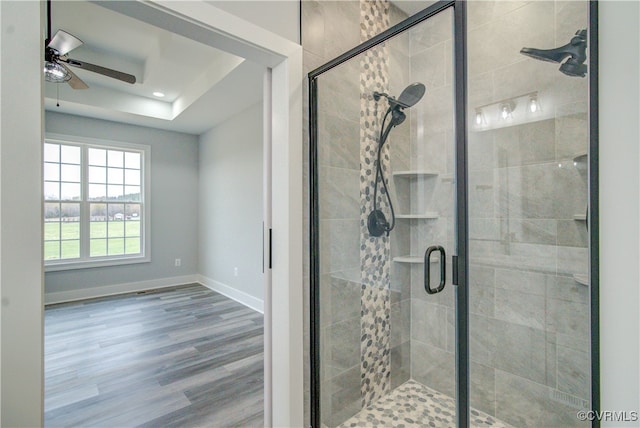 bathroom with ceiling fan, a raised ceiling, wood-type flooring, and walk in shower