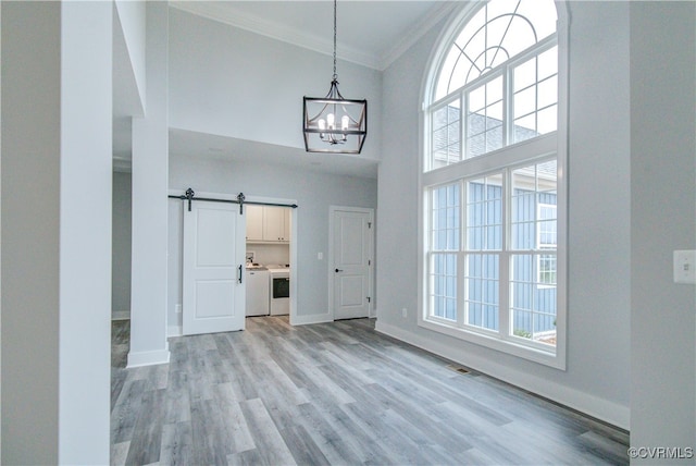 foyer featuring a towering ceiling, ornamental molding, washer and dryer, a barn door, and light hardwood / wood-style floors