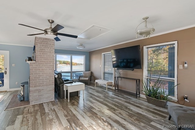 living room featuring ceiling fan, wood-type flooring, ornamental molding, and a wood stove