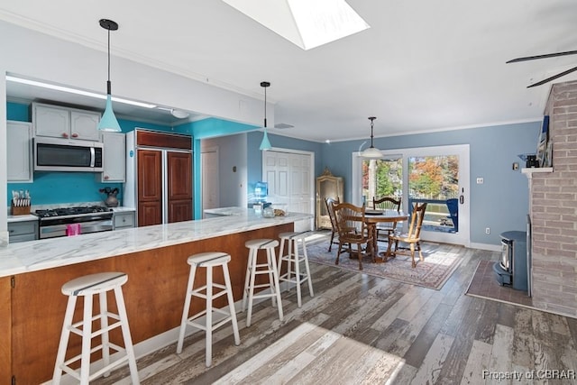 kitchen with light stone countertops, stainless steel appliances, dark hardwood / wood-style floors, crown molding, and a breakfast bar area