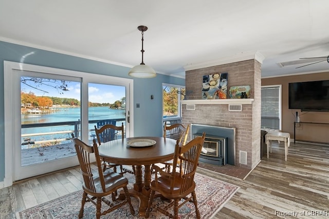 dining space featuring a wood stove, a water view, hardwood / wood-style flooring, ceiling fan, and ornamental molding