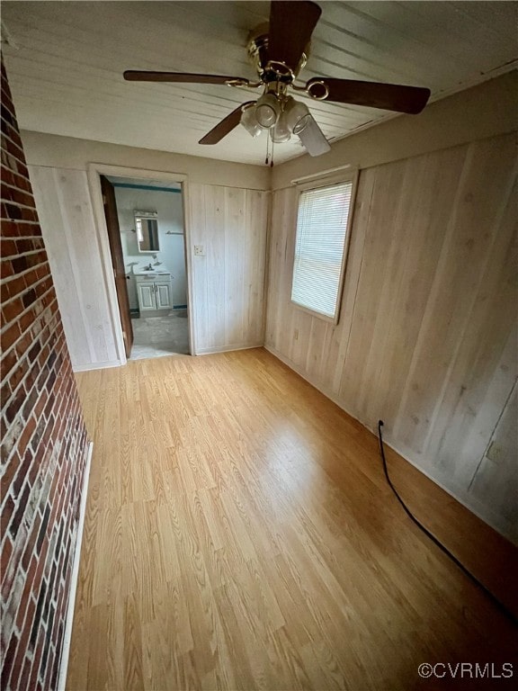 interior space featuring light wood-type flooring, ceiling fan, and wooden walls