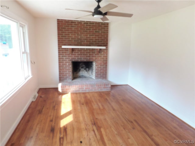 unfurnished living room featuring hardwood / wood-style flooring, ceiling fan, a fireplace, and a wealth of natural light