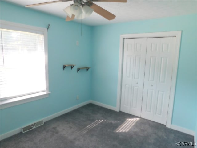 unfurnished bedroom with dark colored carpet, a closet, multiple windows, and ceiling fan