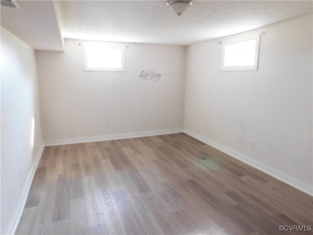 basement featuring a healthy amount of sunlight, light hardwood / wood-style floors, and a textured ceiling