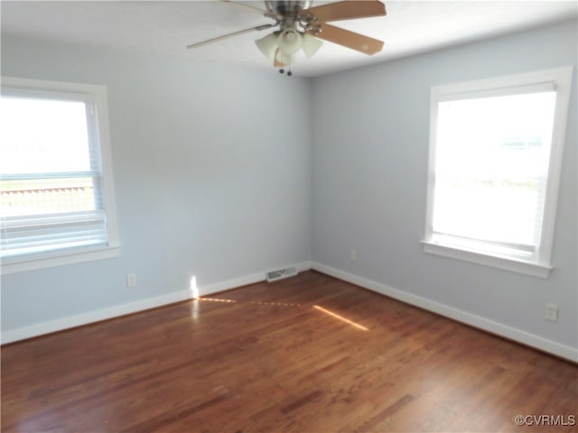 empty room featuring a wealth of natural light, ceiling fan, and dark wood-type flooring