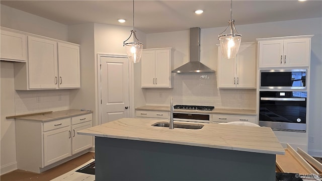 kitchen with decorative light fixtures, an island with sink, wall chimney range hood, and stainless steel appliances