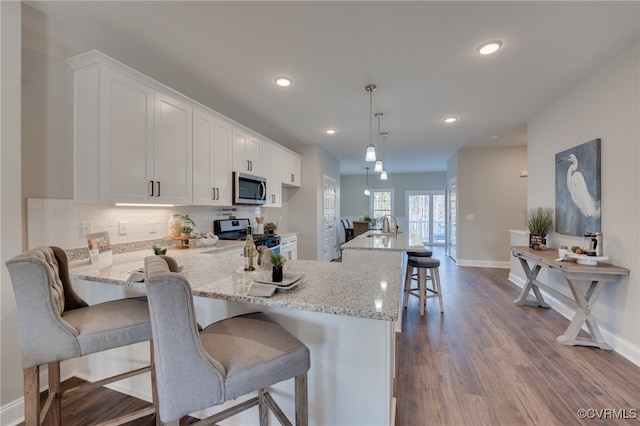 kitchen with pendant lighting, hardwood / wood-style floors, white cabinets, a kitchen breakfast bar, and stainless steel appliances