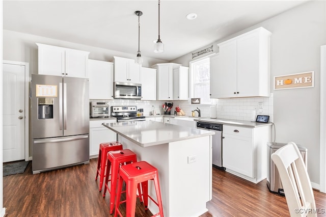 kitchen with white cabinets, dark hardwood / wood-style flooring, a kitchen island, and appliances with stainless steel finishes