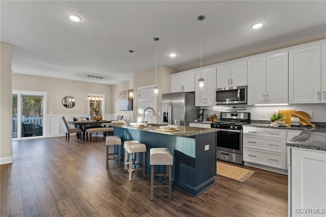 kitchen with white cabinets, appliances with stainless steel finishes, decorative light fixtures, and an island with sink