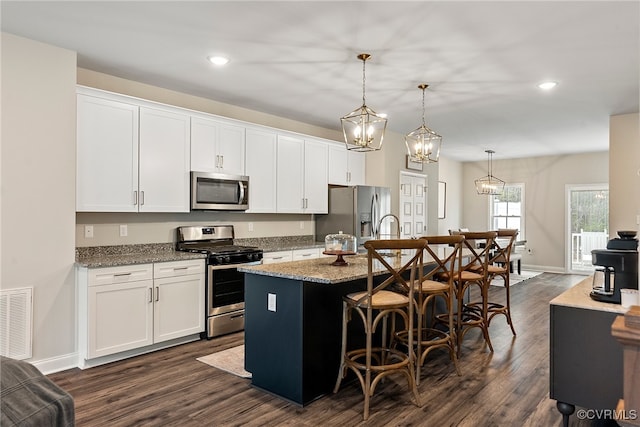 kitchen with a kitchen island with sink, hanging light fixtures, appliances with stainless steel finishes, dark hardwood / wood-style flooring, and white cabinetry