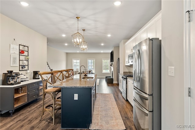 kitchen featuring dark hardwood / wood-style flooring, an island with sink, a kitchen bar, white cabinets, and appliances with stainless steel finishes