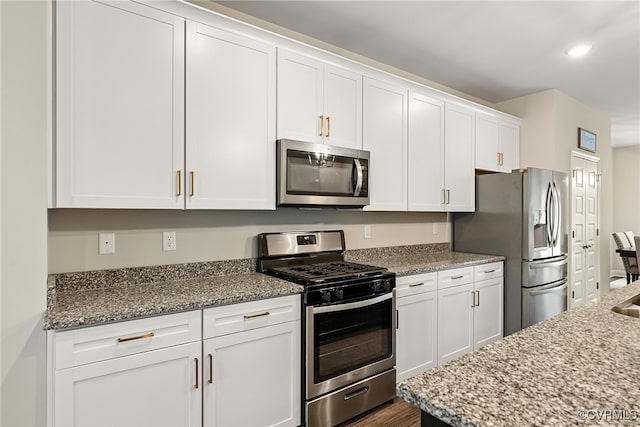 kitchen with light stone counters, white cabinetry, dark wood-type flooring, and appliances with stainless steel finishes