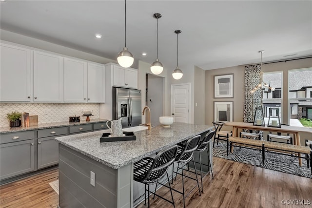 kitchen featuring pendant lighting, stainless steel fridge, light stone countertops, and an island with sink