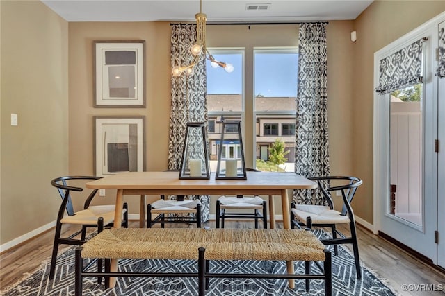 dining area with wood-type flooring, a wealth of natural light, and a notable chandelier