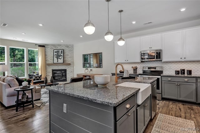 kitchen with appliances with stainless steel finishes, white cabinetry, hanging light fixtures, a kitchen island with sink, and light stone counters