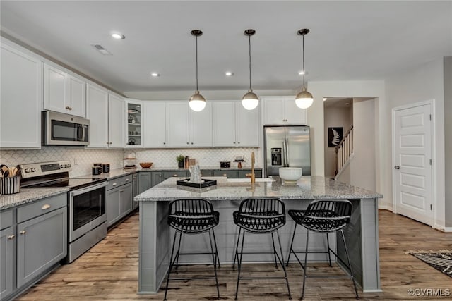 kitchen featuring decorative light fixtures, a center island with sink, gray cabinets, and appliances with stainless steel finishes