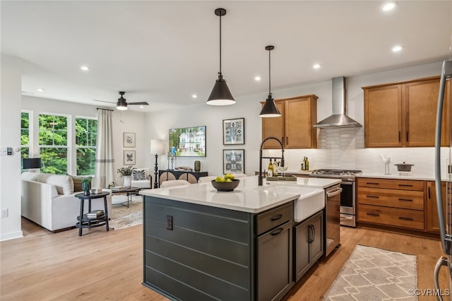 kitchen with tasteful backsplash, a center island with sink, decorative light fixtures, stainless steel range with gas cooktop, and wall chimney exhaust hood