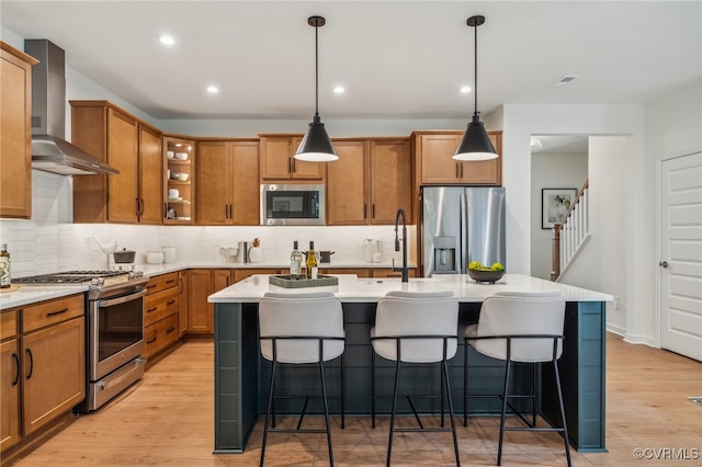 kitchen featuring pendant lighting, appliances with stainless steel finishes, an island with sink, and wall chimney range hood