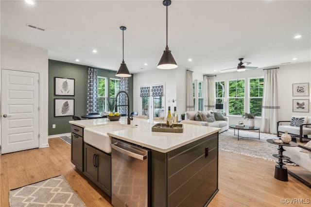 kitchen featuring decorative light fixtures, dishwasher, an island with sink, sink, and light wood-type flooring